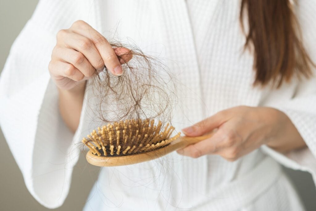 woman looking at brush full of sheeded hair as she experiences hair loss 
