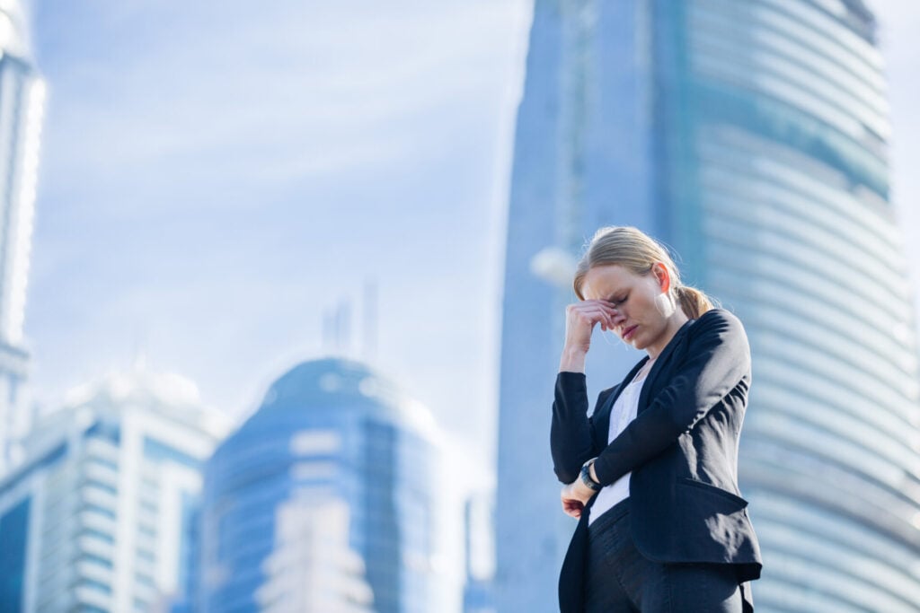 Business leaders holding head clearly bothered by the burden of work with skyscrapers in background 