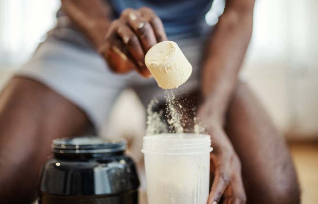 Young man preparing a nutrient supplement drink, pouring protein powder or creatine with a scoop into a shaker bottle after a workout for muscle recovery and fitness goals
