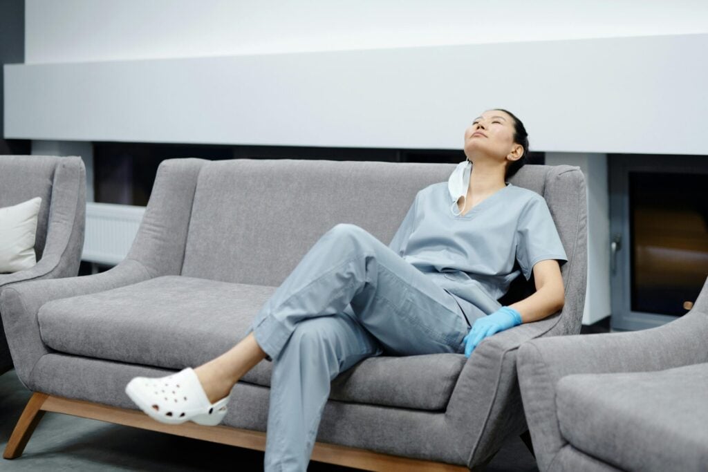 A healthcare worker lying back on a sofa looks exhausted. Nurse burnout 