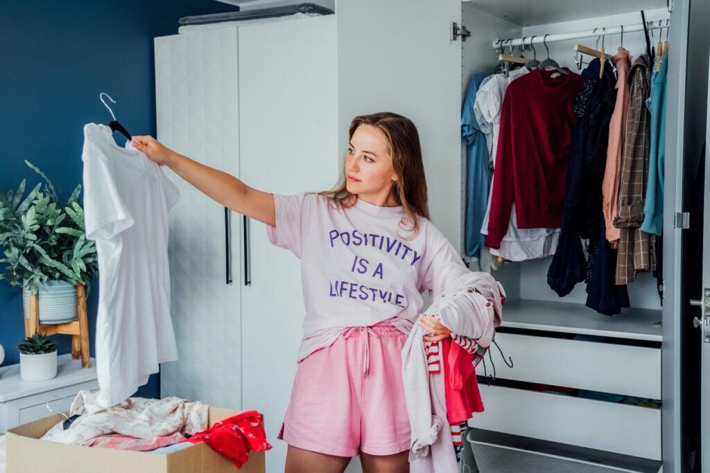 Woman selecting clothes from her wardrobe for donating to a Charity shop. Decluttering, Sorting clothes and Cleaning Up. Reuse, second-hand concept. Conscious consumer, sustainable lifestyle