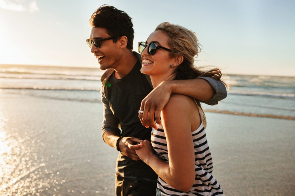 Outdoor shot of smiling young couple walking on beach. Young man and woman strolling together on seashore on a summer day