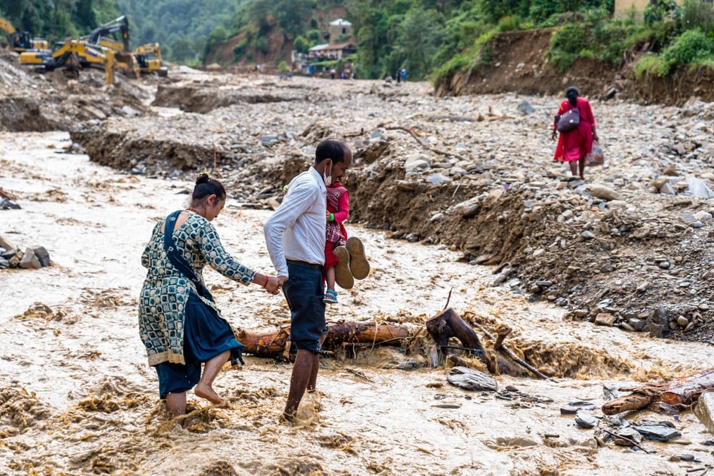 Man carrying his child and wife through the debris after flash floods in Nepal 