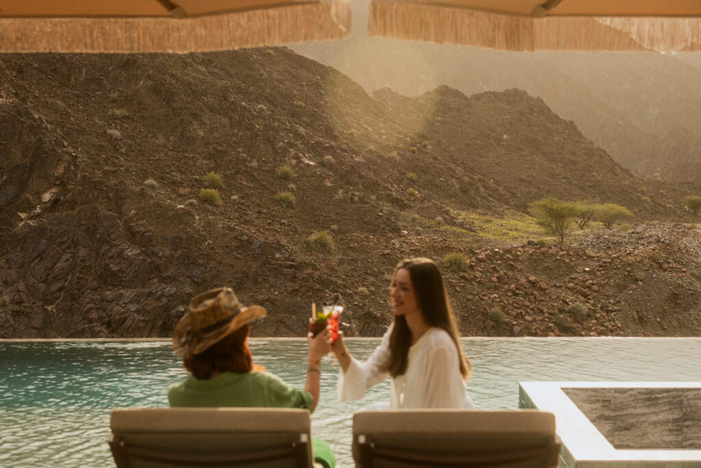 Women saying cheers with drinks by the pool in the mountains at Caravan Hatta by Our Habitas