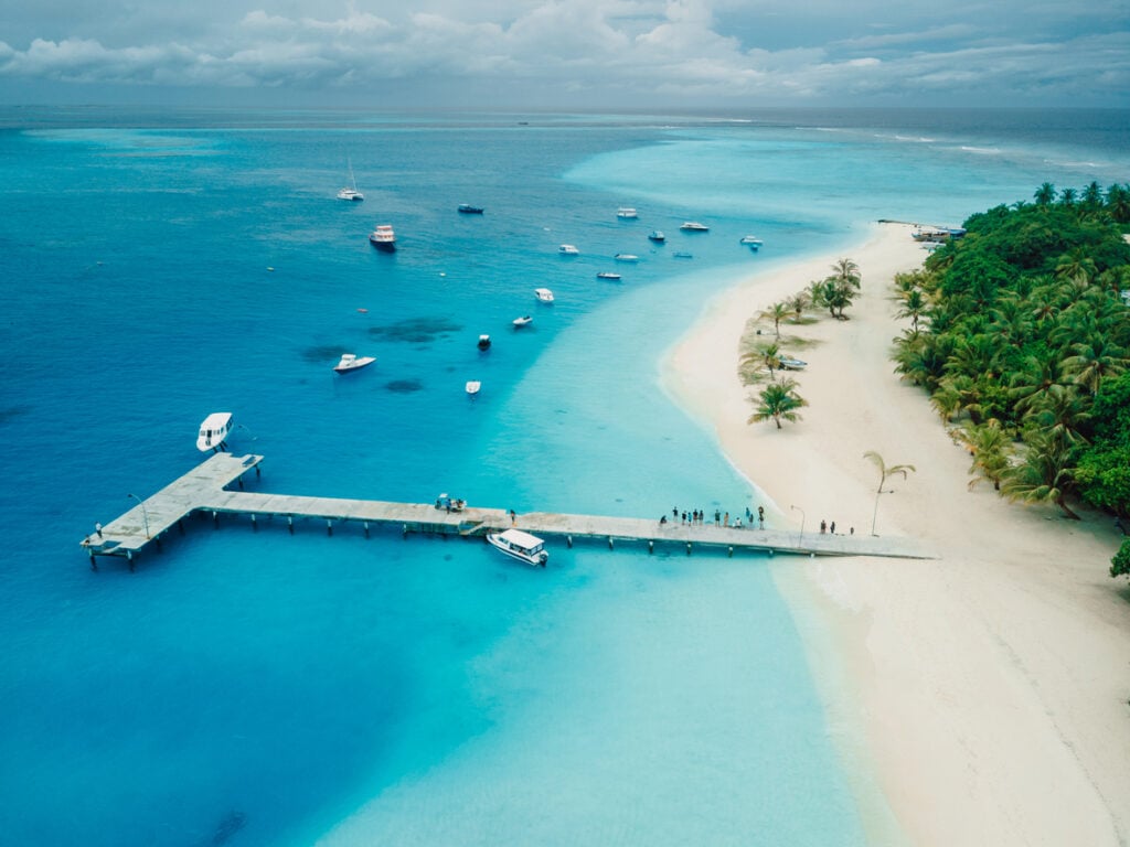 Maldives tropical beach with pier and touristic boats on Fulidhoo island. Travel vacation concept, drone shot