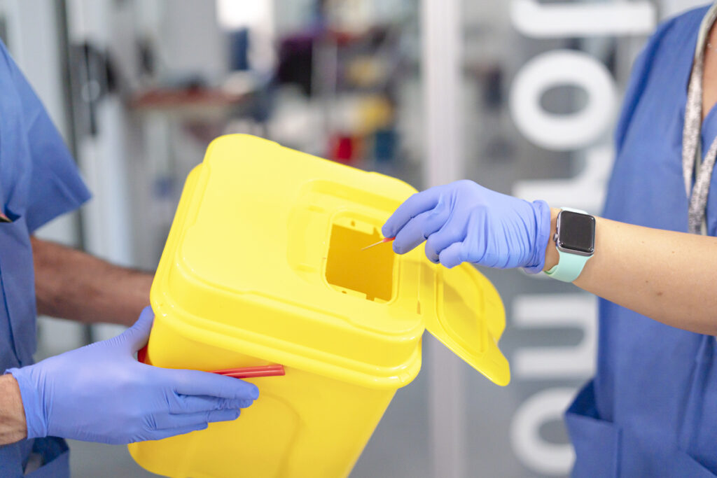 Medical professional safely discarding used syringe in designated sharps container, highlighting proper biohazard waste management in healthcare