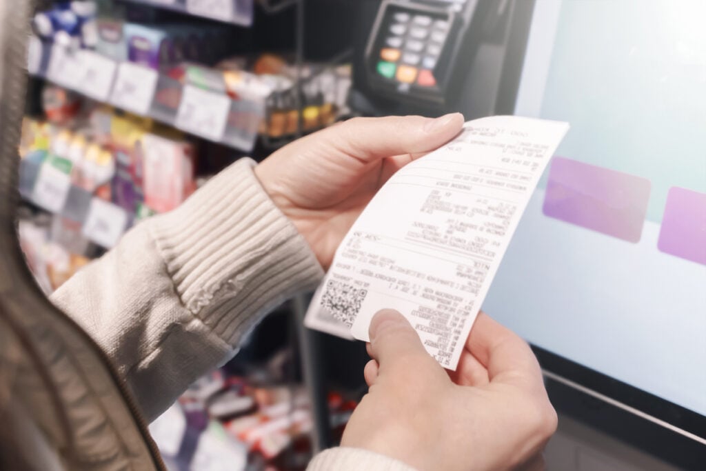 In Choithrams, a woman examines her receipt at a self-service checkout. She focuses on managing her family budget and tracking shopping expenses efficiently