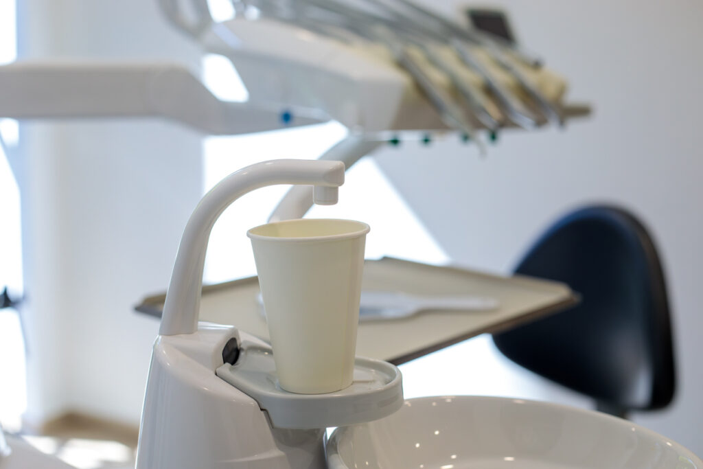 Dental chair rinse cup holder with paper cup and dentist tools in blurred background. Modern dentistry equipment concept